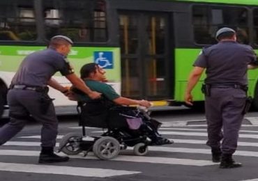 Policiais ajudam cadeirante a atravessar a rua.